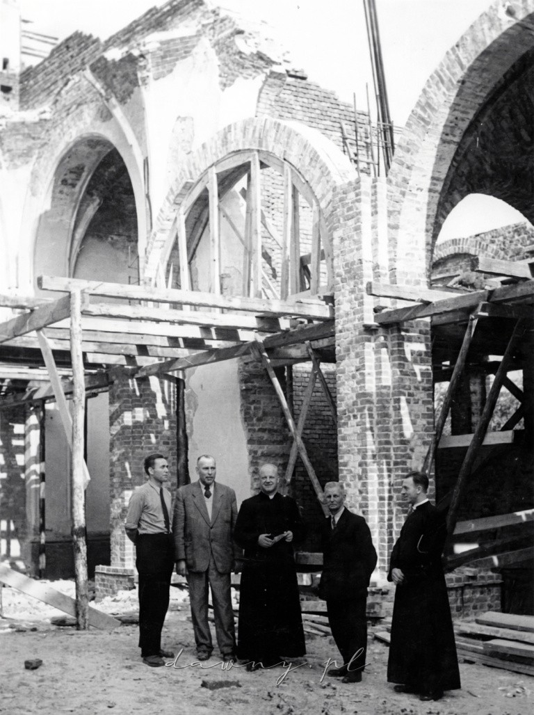 Księża i cywile na tle odbudowywanego kościoła w Wołominie