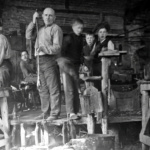 Warsztat huty szkła w Tłuszczu. Butelkę dmucha majster Bolesław Krawczyk, obok stoi pomocnik Stefan Krawczyk, w głębi siedzi Kazimierz Krawczyk.